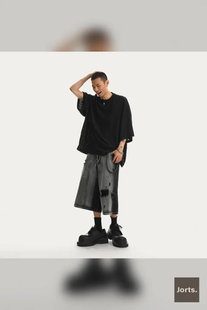 Model wearing mens distressed black denim jorts, showing the mid-rise and straight-leg fit.